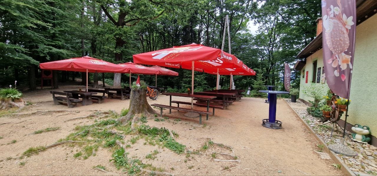 Zunanje mize in rdeči senčniki pri Koči Klobuk